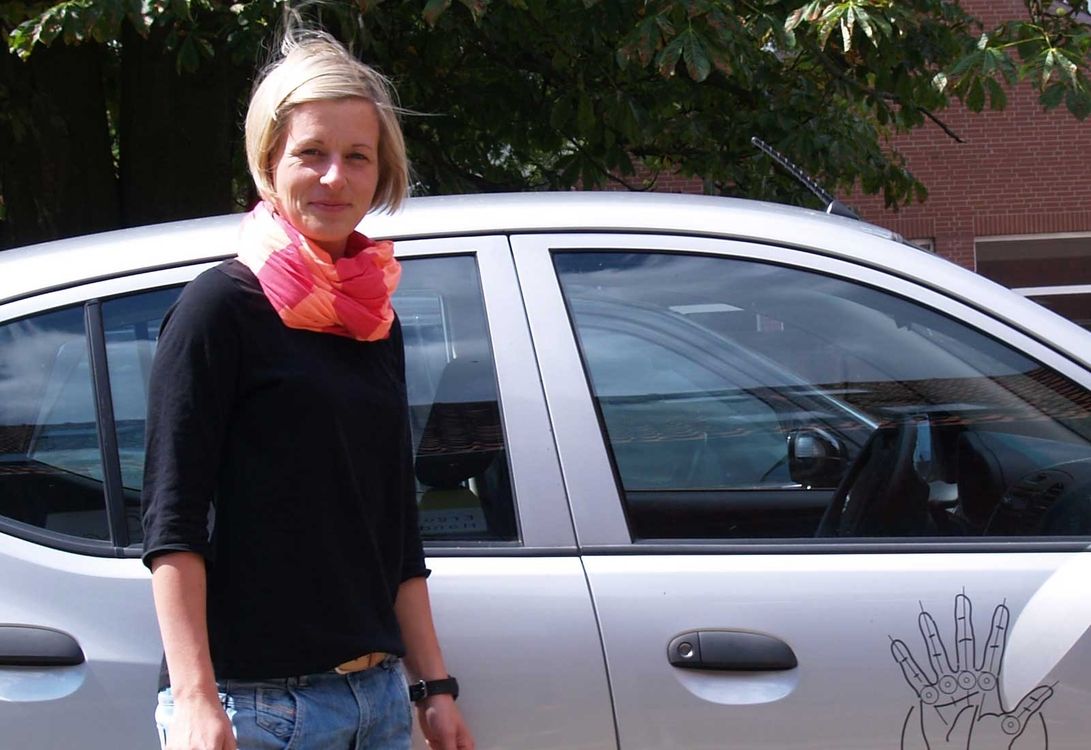 Carola steht vor einem Auto mit dem Logo von Ergo Vital