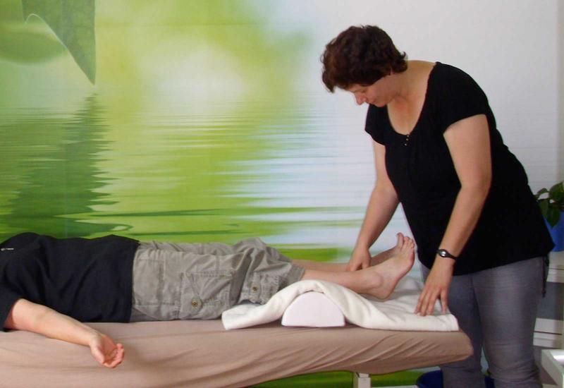 Eine Frau massiert einen liegenden Mann an den Beinen